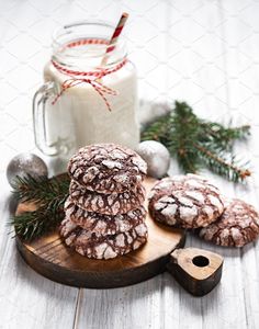 cookies with powdered sugar on a wooden board next to a jar of milk and christmas decorations