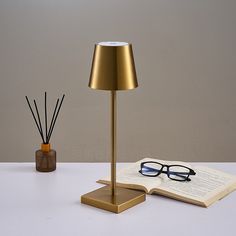 an open book with glasses on it next to a lamp