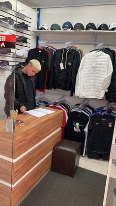 a man standing in front of a wooden counter next to a shelf filled with clothes