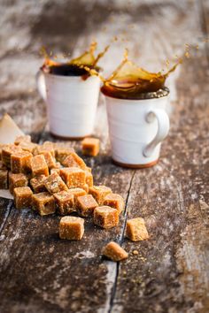 two mugs filled with brown sugar next to each other on a wooden table,