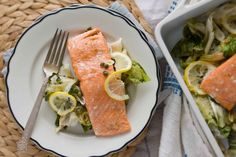 a white plate topped with salmon next to a bowl filled with salad and a fork