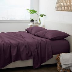 a bed with red sheets and pillows next to a potted plant in a white room