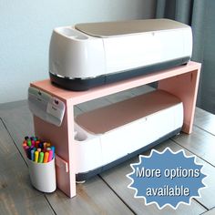 a printer sitting on top of a wooden table next to a cup filled with colored pencils