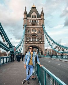 a man walking across a bridge in front of a tall tower with a clock on it