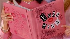 a woman is holding a pink book with the words burn book written in black on it