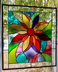 a colorful stained glass window hanging in front of a tree with leaves and flowers on it