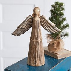 a wooden angel figurine next to a small pine tree on a blue table