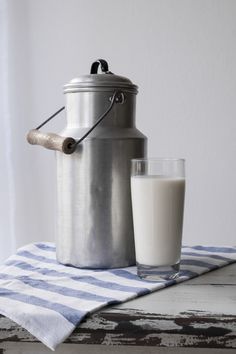 milk being poured into a large metal jug next to a glass of milk