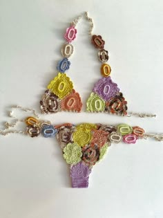 two pieces of crochet are hanging on a white surface, one is multicolored and the other has beads