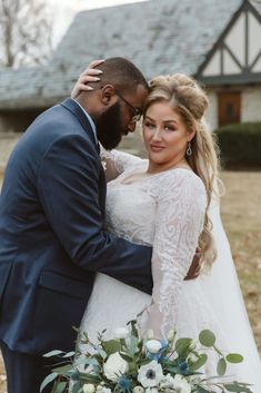 a bride and groom embracing each other in front of a house with a large bouquet