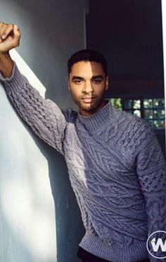 a man leaning against a wall wearing a sweater