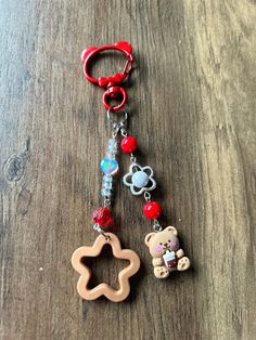 a key chain with two teddy bears attached to it on a wooden surface, one has a red plastic clip and the other has a bear charm