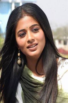 a woman with long black hair and earrings on her head looking at the camera while standing in front of a building