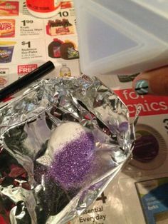 an ice cube is covered in purple glitter and sits on top of some newspaper paper