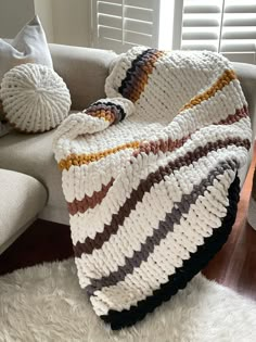 a crocheted blanket sitting on top of a white couch next to two pillows