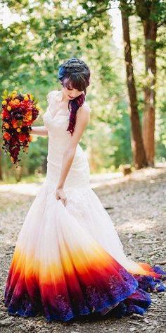 a woman in a wedding dress holding a bouquet and looking at the ground with trees behind her