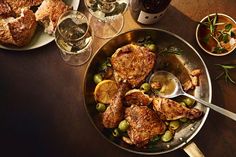 a pan filled with meat and olives on top of a table next to wine glasses