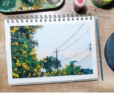 a notebook sitting on top of a wooden table next to paint supplies and a brush