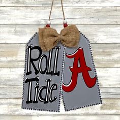 a sign with a bow hanging from it's side on a wooden background that says roll tide