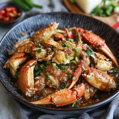 a black bowl filled with cooked crabs covered in sauce and garnished with green onions