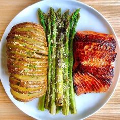 a white plate topped with meat and asparagus on top of a wooden table