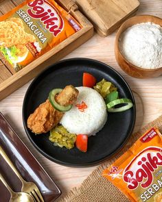 a black plate topped with rice and veggies next to two boxes of chips