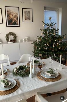 a dining room table set for christmas with white plates and silverware on the placemats