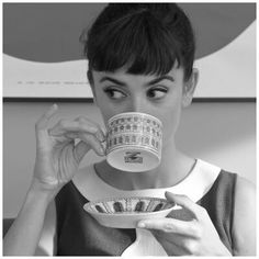 a woman drinking from a coffee cup with money in front of her face and holding a plate