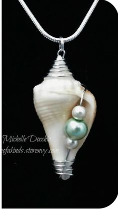 a white shell with two green pearls hanging from it's side on a silver chain