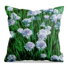 a green and white pillow with purple flowers on the front, along with grass in the background