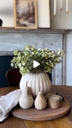 a wooden table topped with a white vase filled with flowers and pears on top of it