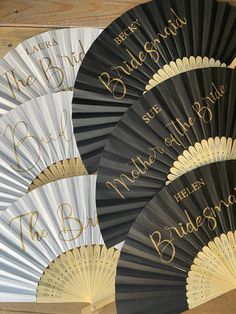 four black and white fans with gold lettering on them are sitting on a wooden surface