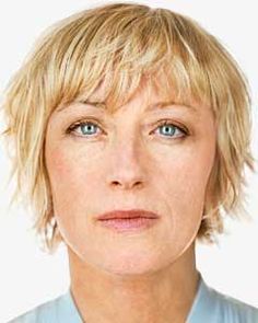 a woman with blonde hair and blue eyes looks at the camera while wearing a collared shirt