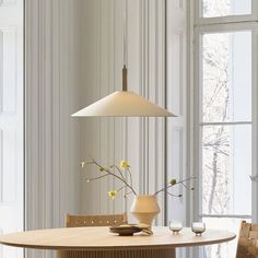 a dining room table with a vase and flowers on it in front of a window