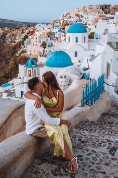 a man and woman sitting on a wall kissing