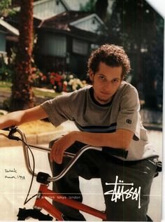 a young man riding a red bike down a street next to a palm tree and houses