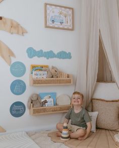 a young boy sitting on the floor in his bedroom with toys and decorations around him