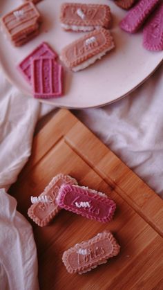 some pink and white cookies on a wooden cutting board next to a plate with one cut in half