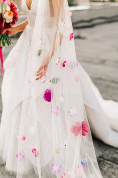 the bride is walking down the street with her bouquet in hand and veil over her head