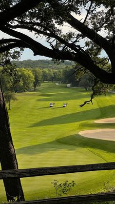 an image of a golf course taken from behind a wooden fence with trees in the foreground