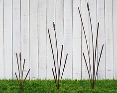 three metal planters sitting in the grass near a white fence with wooden posts sticking out of it