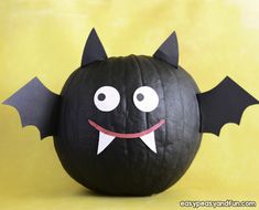 a black pumpkin decorated like a bat sitting on top of a yellow surface with its mouth open