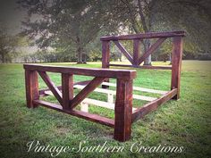 a wooden bed frame sitting on top of a lush green grass covered field with trees in the background