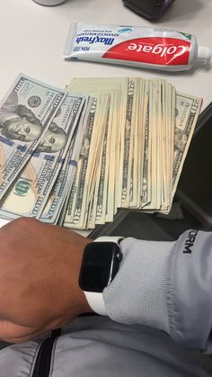 a person holding an apple watch on their wrist with money next to it and toothpaste