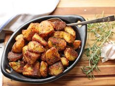 a black bowl filled with fried potatoes on top of a wooden cutting board next to garlic