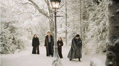 four people standing in the snow next to a lamp post