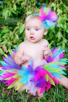 a baby sitting in the grass wearing a colorful tutu