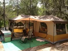 a tent is set up in the woods with chairs and tables around it for camping