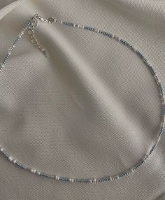 a white and blue beaded necklace laying on top of a cloth