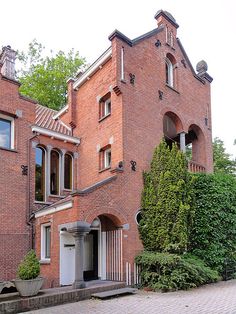 an old brick building with many windows and bushes on the side walk in front of it